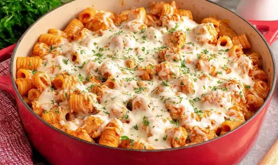 Baked chicken parmesan pasta in a white baking dish with melted mozzarella and fresh basil