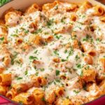 Baked chicken parmesan pasta in a white baking dish with melted mozzarella and fresh basil