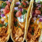 Crispy baked chicken tacos on a baking sheet with melted cheese and fresh toppings