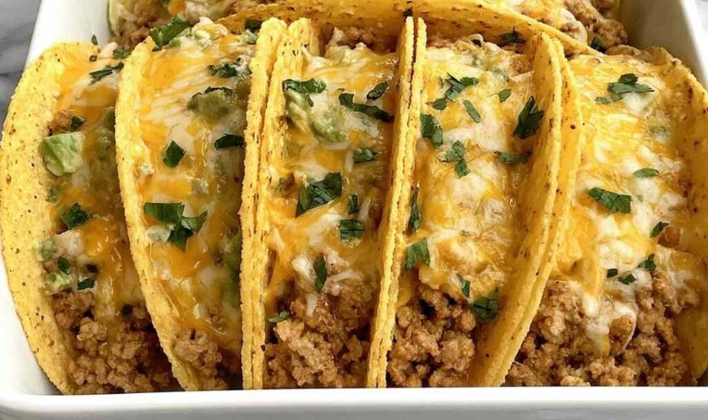 Baked ground chicken tacos in a white baking dish topped with melted cheese and fresh cilantro