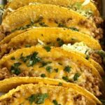 Baked ground chicken tacos in a white baking dish topped with melted cheese and fresh cilantro