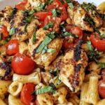 Bruschetta chicken pasta in a white bowl topped with fresh cherry tomatoes and basil