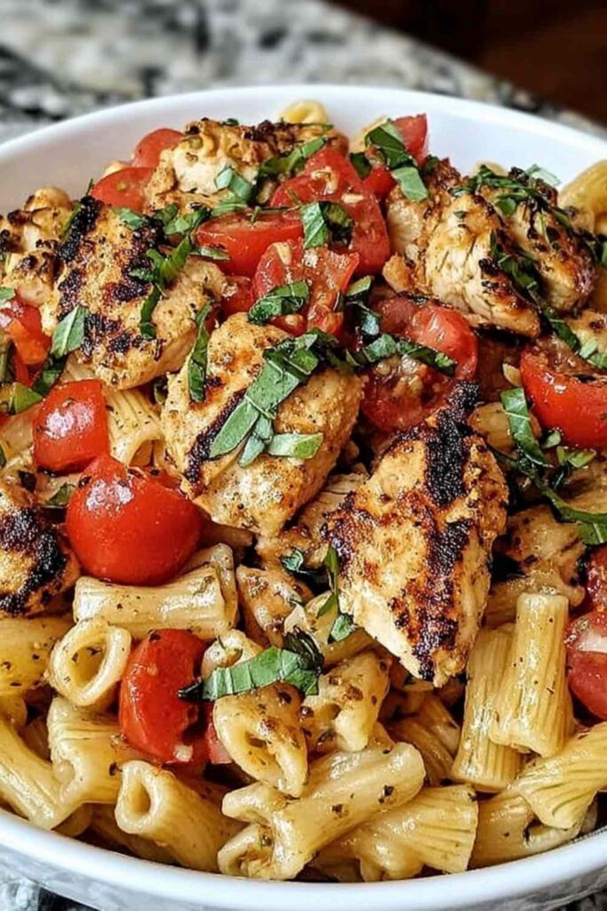 Bruschetta chicken pasta in a white bowl topped with fresh cherry tomatoes and basil