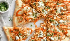 Buffalo chicken ranch pizza on a wooden cutting board with ranch drizzle and green onion garnish