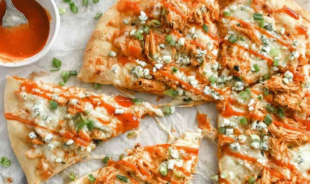 Buffalo chicken ranch pizza on a wooden cutting board with ranch drizzle and green onion garnish
