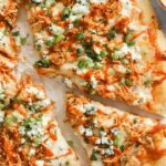Buffalo chicken ranch pizza on a wooden cutting board with ranch drizzle and green onion garnish