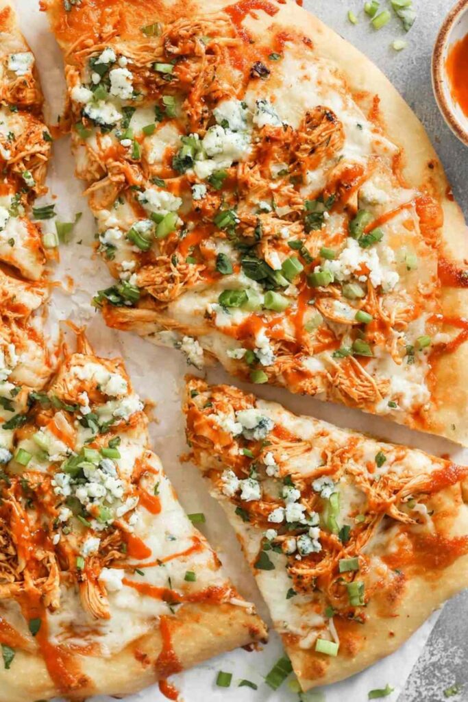 Buffalo chicken ranch pizza on a wooden cutting board with ranch drizzle and green onion garnish