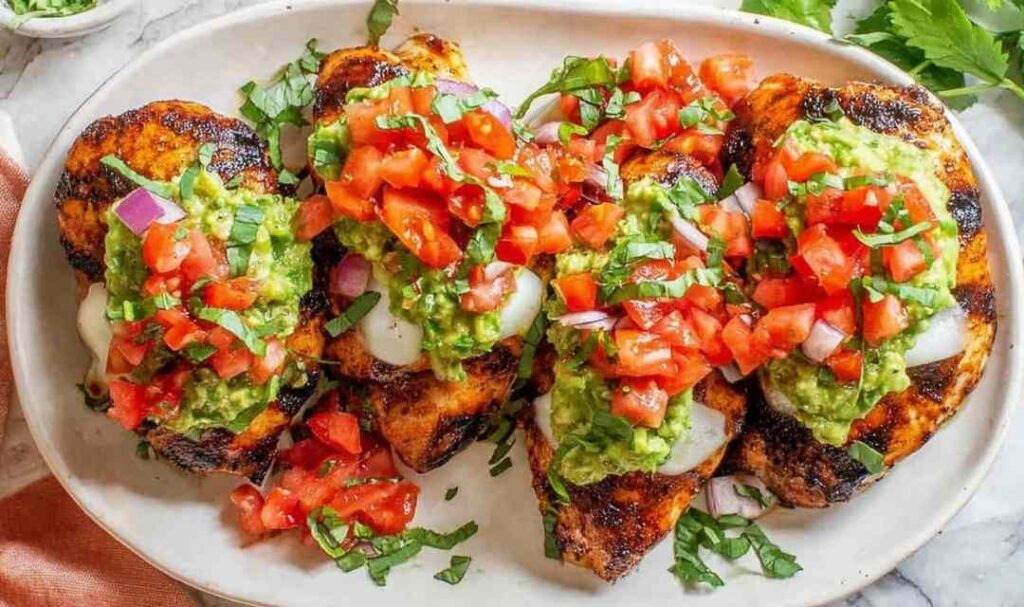 California grilled chicken topped with creamy avocado, melted fresh mozzarella, and fresh tomatoes on a white plate