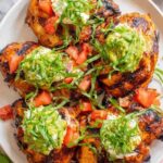 California grilled chicken topped with creamy avocado, melted fresh mozzarella, and fresh tomatoes on a white plate