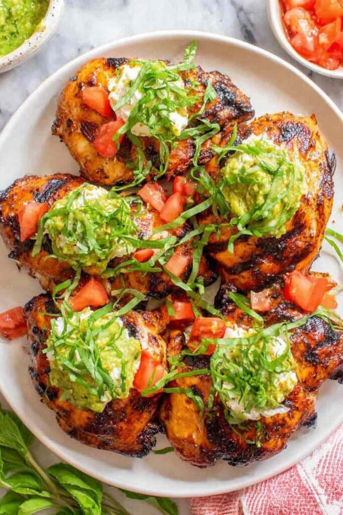 California grilled chicken topped with creamy avocado, melted fresh mozzarella, and fresh tomatoes on a white plate
