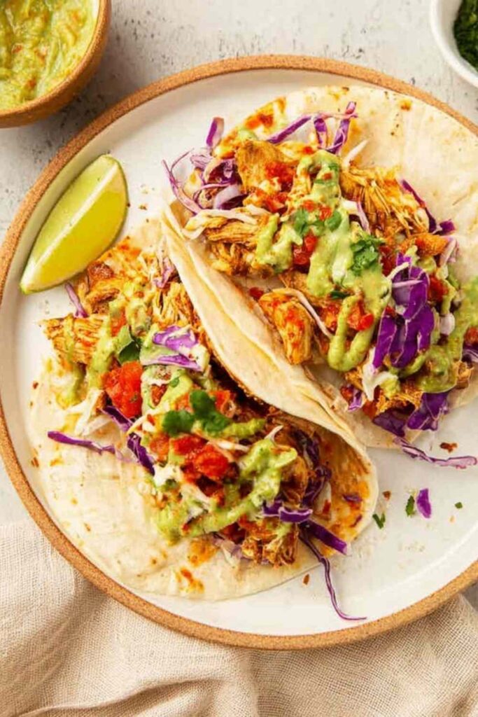 Homemade cantina chicken tacos with juicy shredded chicken, pico de gallo, avocado salsa verde, and cheddar cheese on warm flour tortillas