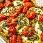 Caprese chicken casserole in a white baking dish with golden melted mozzarella and halved cherry tomatoes