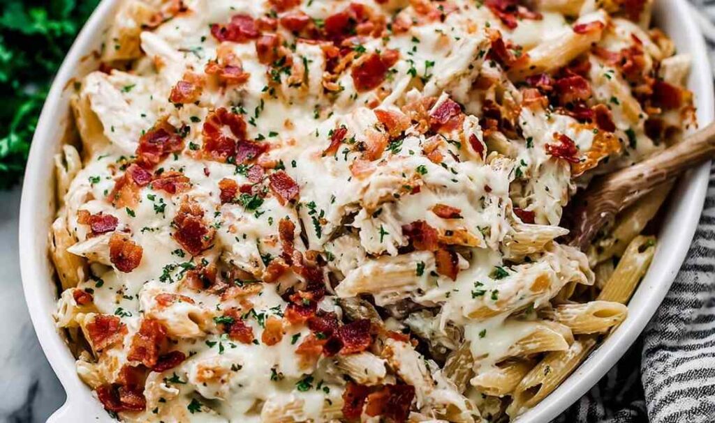 Chicken Bacon Ranch Pasta Bake in a white 9x13 casserole dish with golden melted mozzarella and crispy chopped bacon on top
