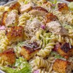 Chicken Caesar pasta salad with ground beef in a large white bowl topped with Parmesan cheese