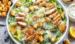 Chicken Caesar salad with grilled chicken slices, crisp romaine lettuce, golden Parmesan croutons, and shredded Parmesan on a white plate