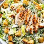 Chicken Caesar salad with grilled chicken slices, crisp romaine lettuce, golden Parmesan croutons, and shredded Parmesan on a white plate