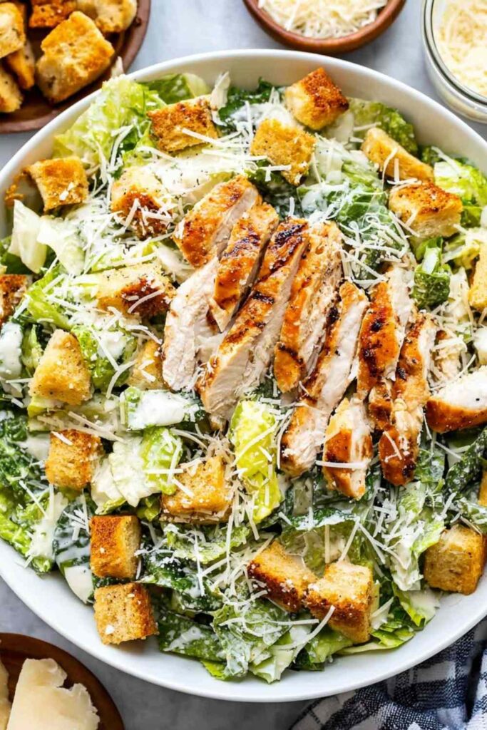 Chicken Caesar salad with grilled chicken slices, crisp romaine lettuce, golden Parmesan croutons, and shredded Parmesan on a white plate