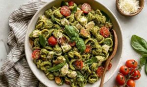 Chicken pesto pasta salad in a large white bowl with cherry tomatoes, cucumber, and fresh basil