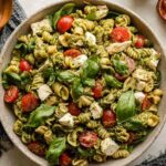 Chicken pesto pasta salad in a large white bowl with cherry tomatoes, cucumber, and fresh basil