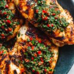 Grilled chimichurri chicken breasts topped with fresh parsley herb sauce on a white plate