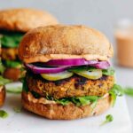 Classic lentil burgers served on a whole grain bun with lettuce, tomato, and avocado on a wooden board