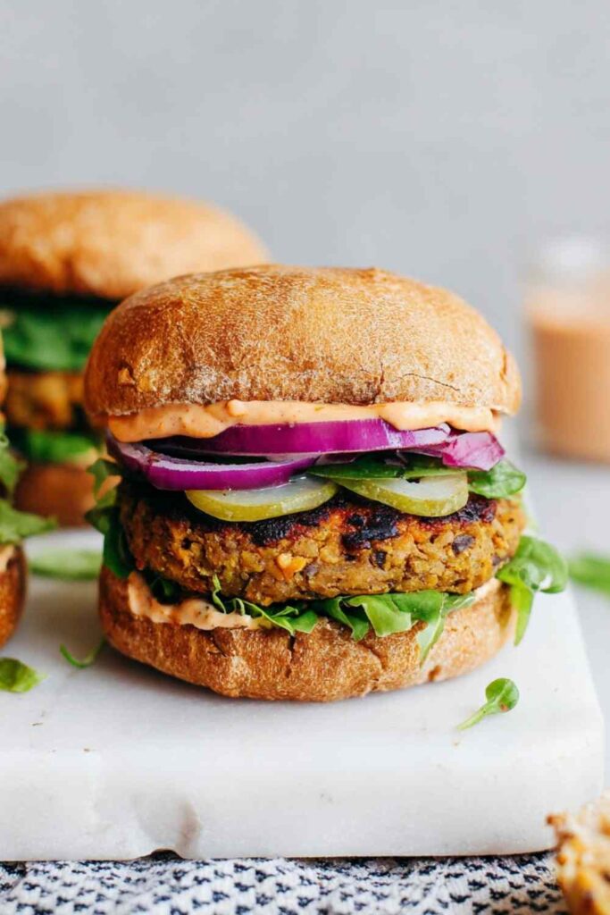 Classic lentil burgers served on a whole grain bun with lettuce, tomato, and avocado on a wooden board