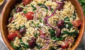 Costco copycat orzo salad in a large serving bowl with feta, salami, olives, and cherry tomatoes
