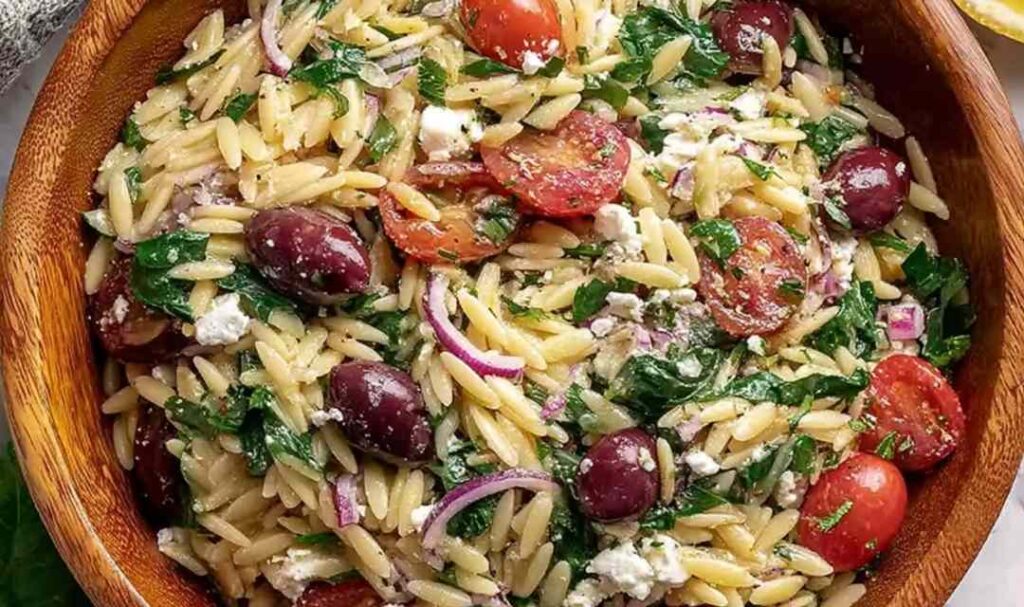 Costco copycat orzo salad in a large serving bowl with feta, salami, olives, and cherry tomatoes