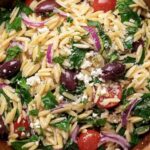Costco copycat orzo salad in a large serving bowl with feta, salami, olives, and cherry tomatoes