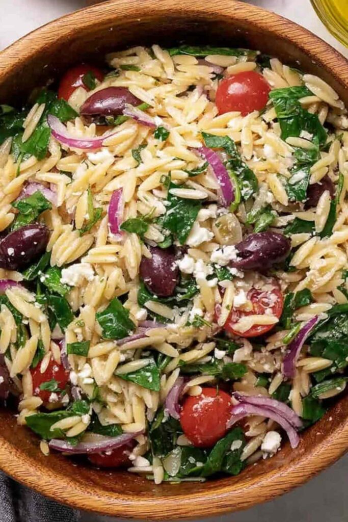 Costco copycat orzo salad in a large serving bowl with feta, salami, olives, and cherry tomatoes