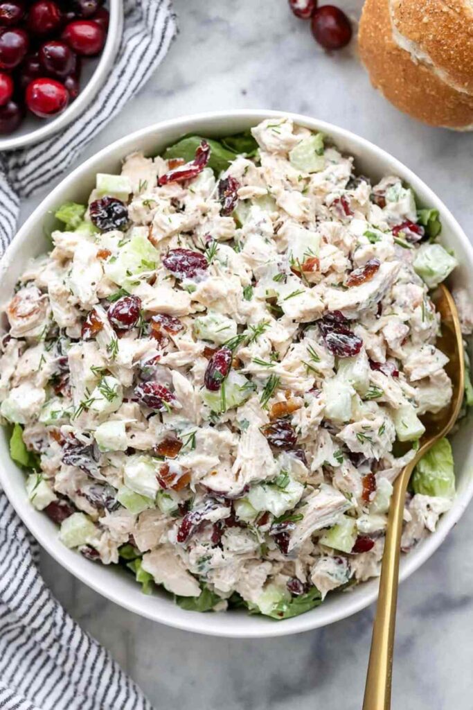 Cranberry chicken salad with dried cranberries, pecans, and apple in a large white bowl