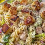 Creamy chicken Caesar pasta salad in a large bowl topped with croutons, Parmesan, and chopped romaine