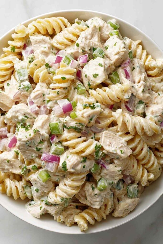 Creamy chicken pasta salad in a large white bowl with fresh parsley garnish