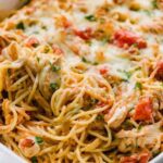 Creamy chicken spaghetti casserole in a white baking dish with golden bubbly mozzarella on top