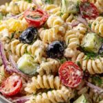 Creamy pasta salad with rotini, cherry tomatoes, cucumber, and fresh dill in a large white bowl