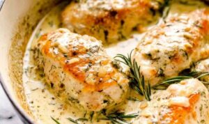 Creamy rosemary chicken breasts in a skillet with herb cream sauce