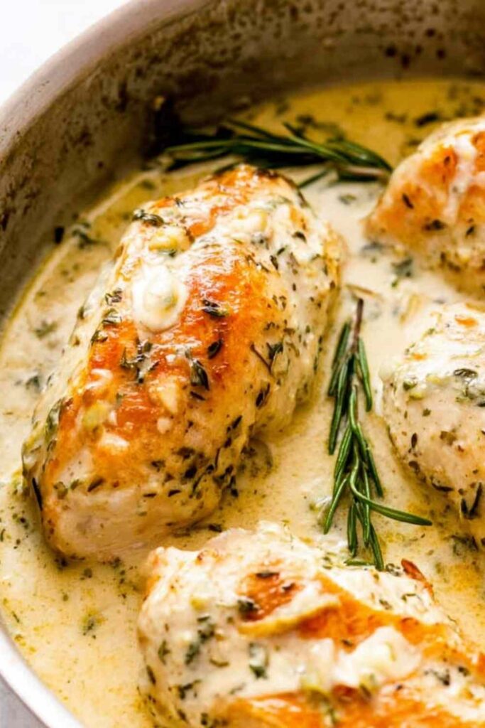 Creamy rosemary chicken breasts in a skillet with herb cream sauce