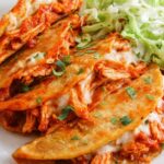 Crispy baked chicken tacos on a parchment-lined sheet pan with golden crunchy corn shells and melted cheese