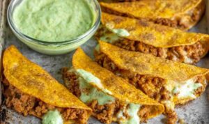 Crispy chicken tacos baked golden on a white plate served with avocado cilantro sauce and lime wedges