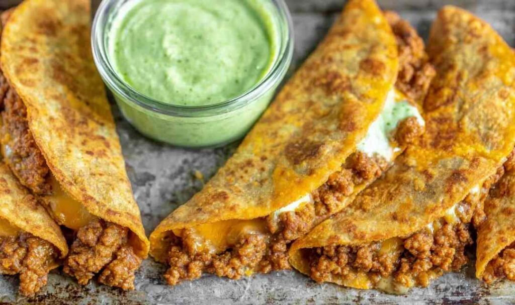 Crispy chicken tacos baked golden on a white plate served with avocado cilantro sauce and lime wedges