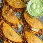 Crispy chicken tacos baked golden on a white plate served with avocado cilantro sauce and lime wedges