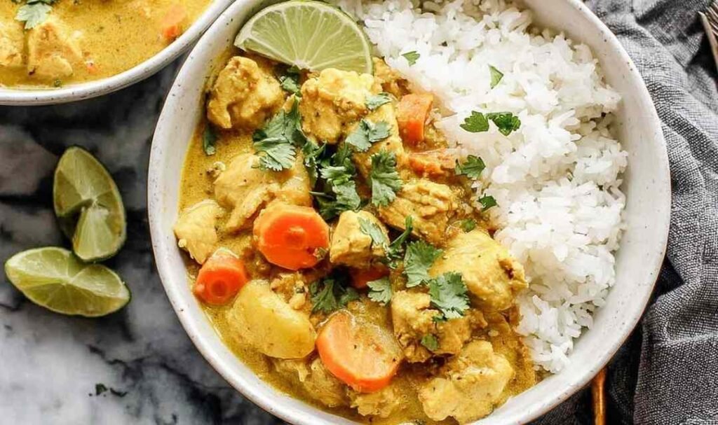 Crockpot curry chicken served over basmati rice in a white bowl topped with fresh cilantro and chopped cashews