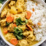 Crockpot curry chicken served over basmati rice in a white bowl topped with fresh cilantro and chopped cashews