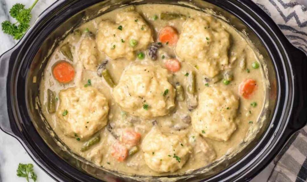 Crockpot chicken and dumplings with fluffy biscuit dumplings in creamy herb broth served in a deep bowl