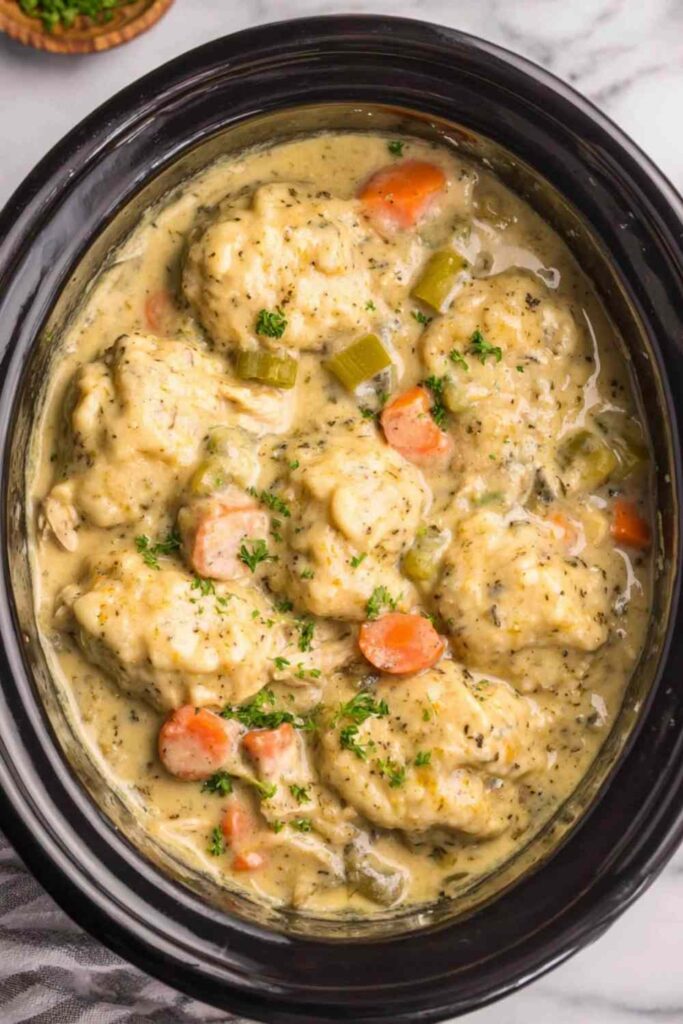 Crockpot chicken and dumplings with fluffy biscuit dumplings in creamy herb broth served in a deep bowl