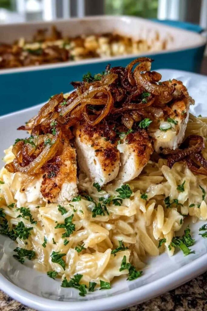 French Onion Chicken Orzo Casserole in a white baking dish with golden bubbly Gruyere cheese topping and fresh parsley garnish