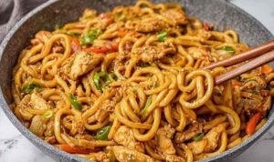 Ginger chicken udon noodles stir fry in a skillet topped with sesame seeds and scallions