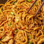 Ginger chicken udon noodles stir fry in a skillet topped with sesame seeds and scallions