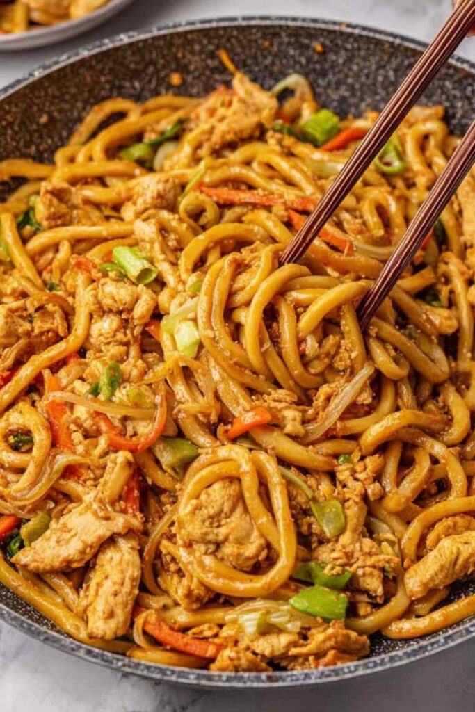 Ginger chicken udon noodles stir fry in a skillet topped with sesame seeds and scallions