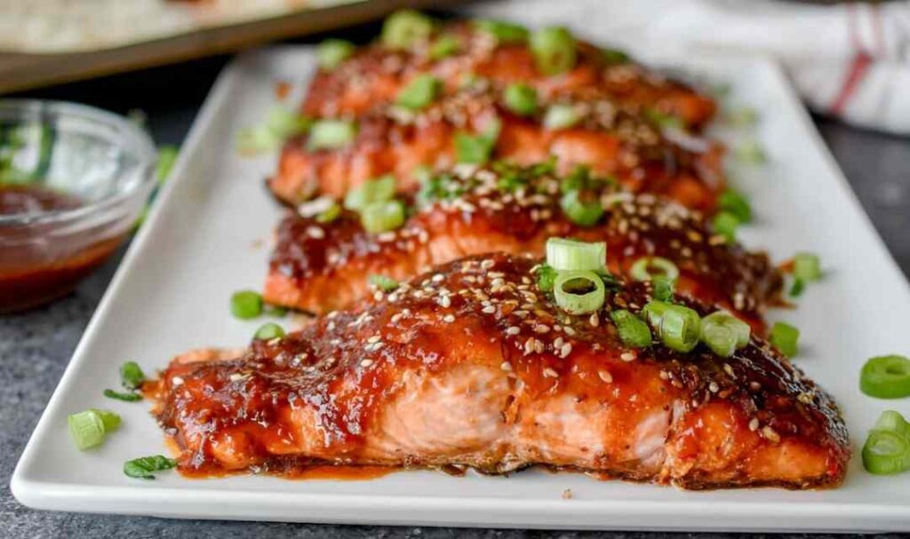Broiled gochujang salmon fillets with caramelized Korean chili glaze, topped with sesame seeds and sliced green onion on a foil-lined baking sheet